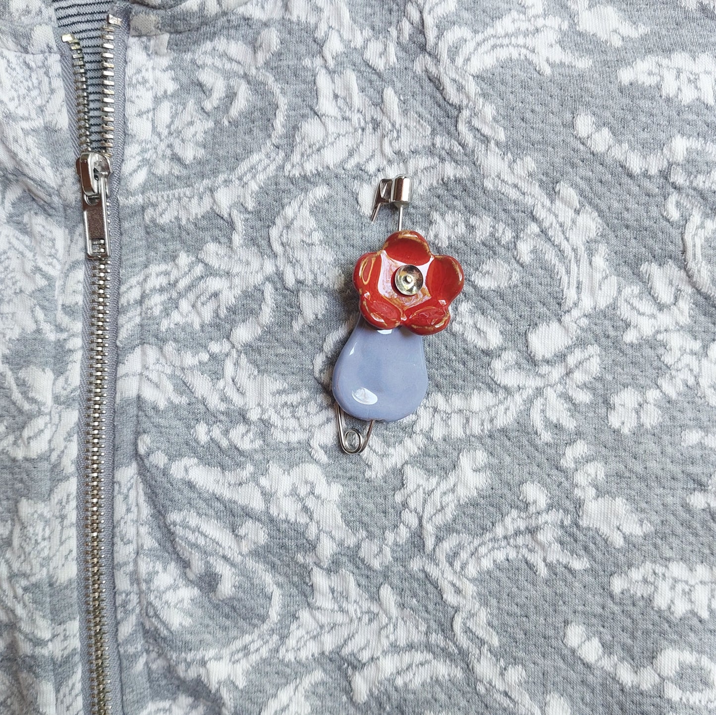 Spilla fiore con vaso in ceramica azzurra e rossa con chiusura in metallo.