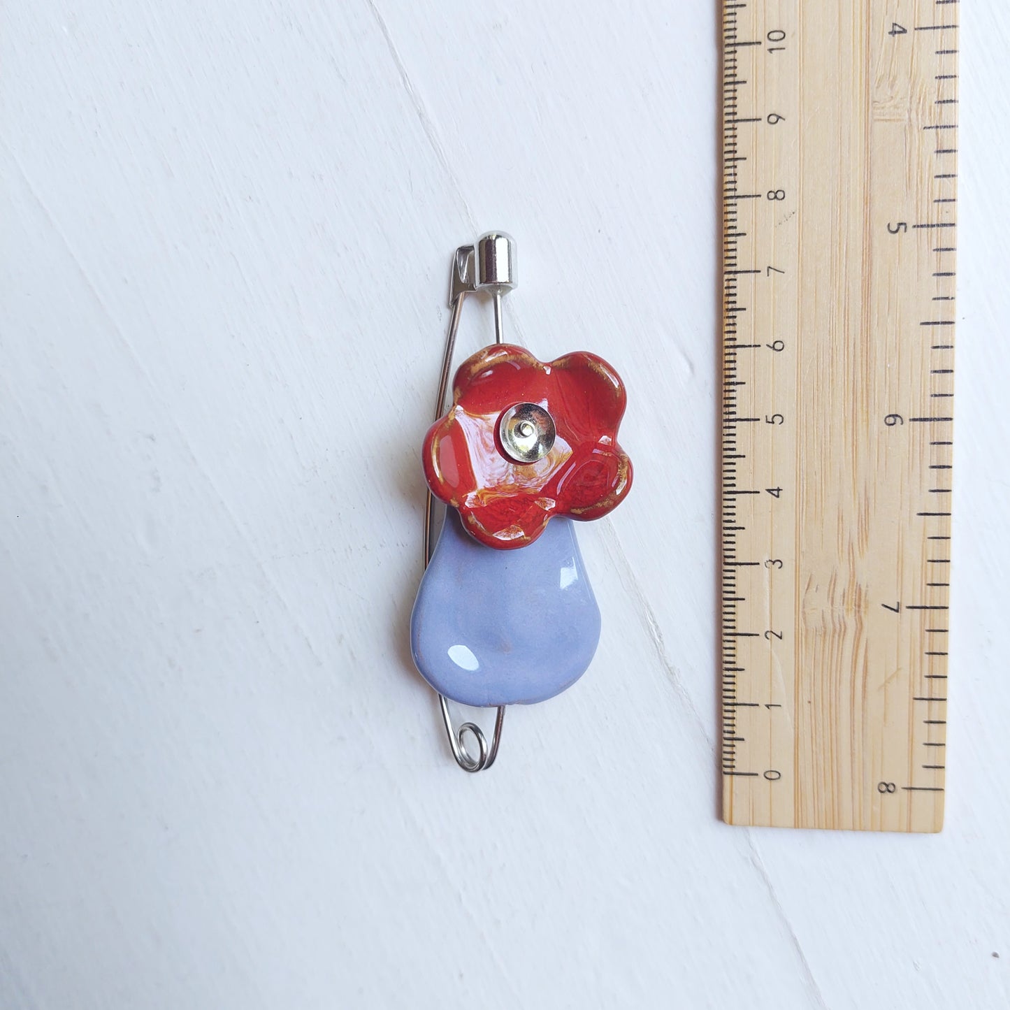 Spilla fiore con vaso in ceramica azzurra e rossa con chiusura in metallo.