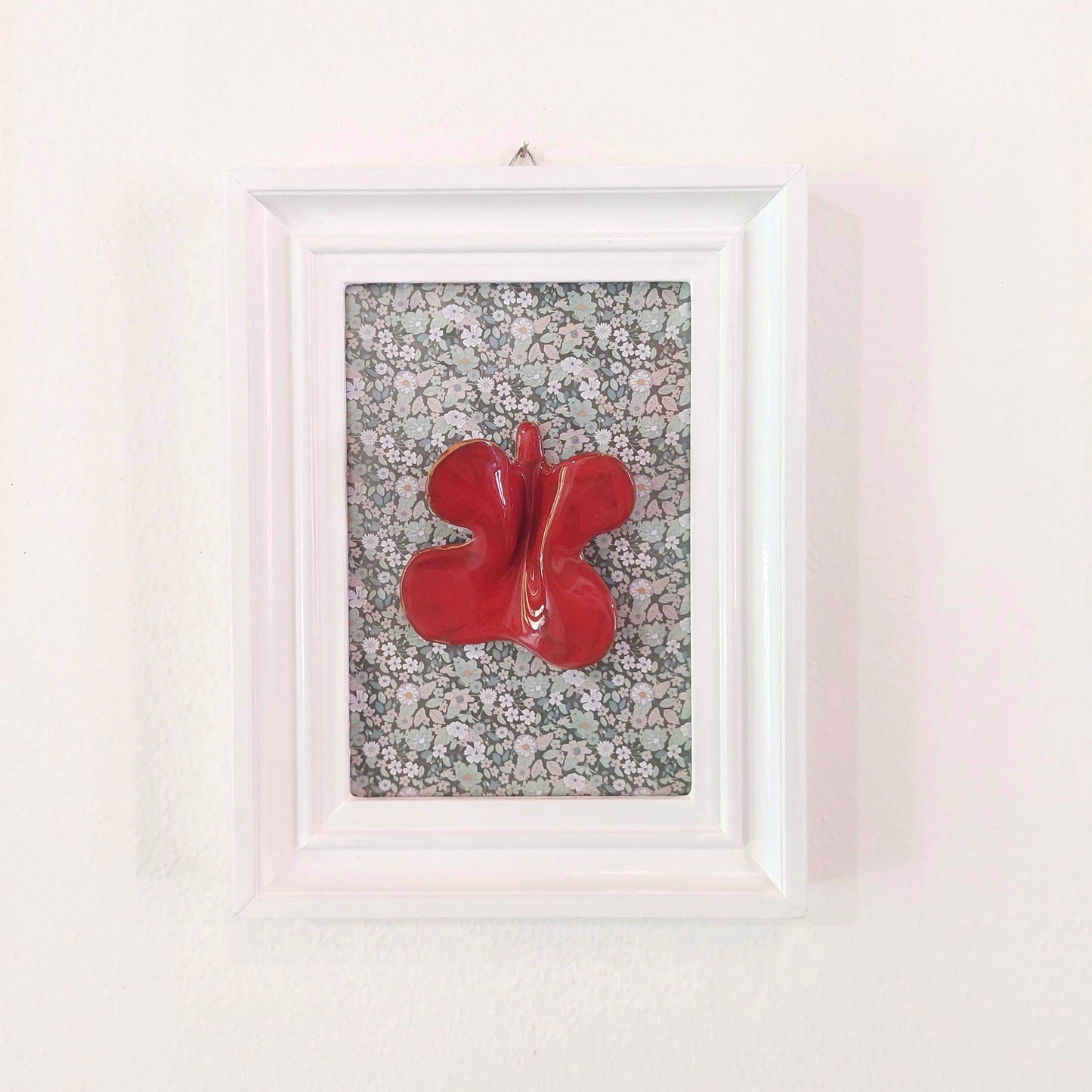 Quadro con farfalla in ceramica rossa e cornice in legno bianco.