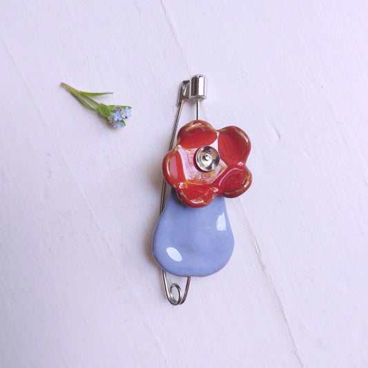 Spilla fiore con vaso in ceramica azzurra e rossa con chiusura in metallo.