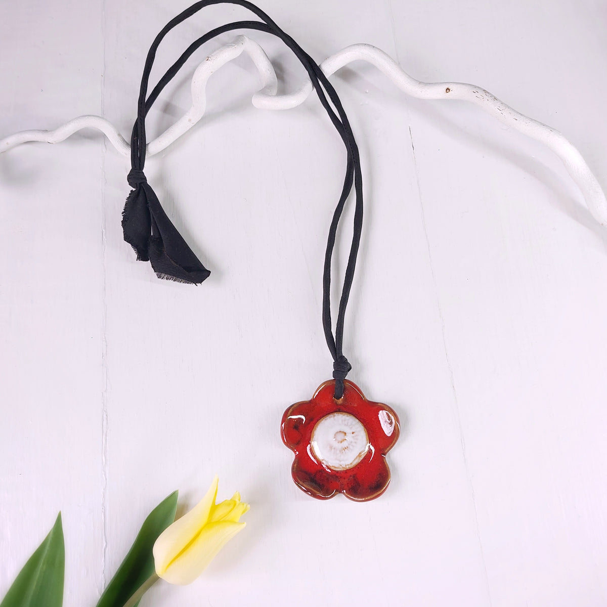Collana con fiore in ceramica rossa e bianca e laccio in seta nera.