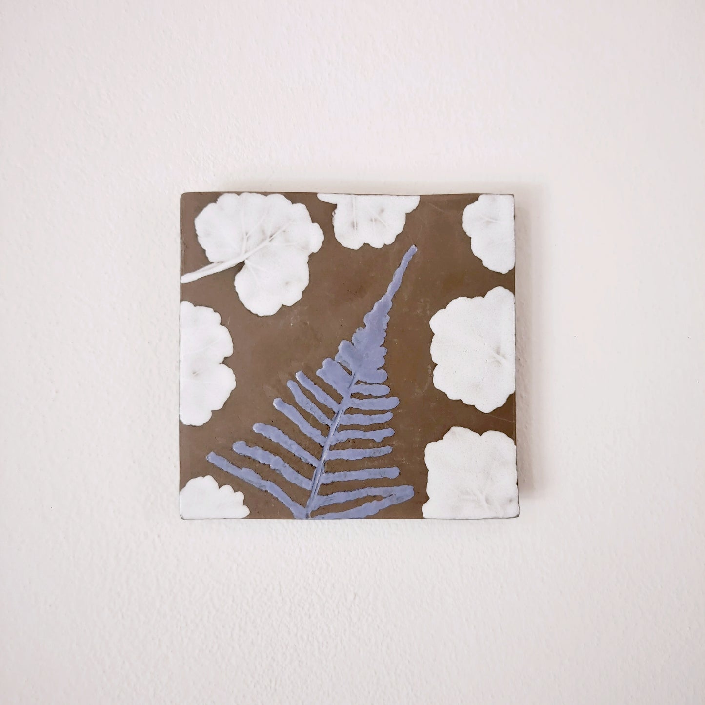 Formella in ceramica con decorazione a foglie azzurre e bianche su fondo marrone.