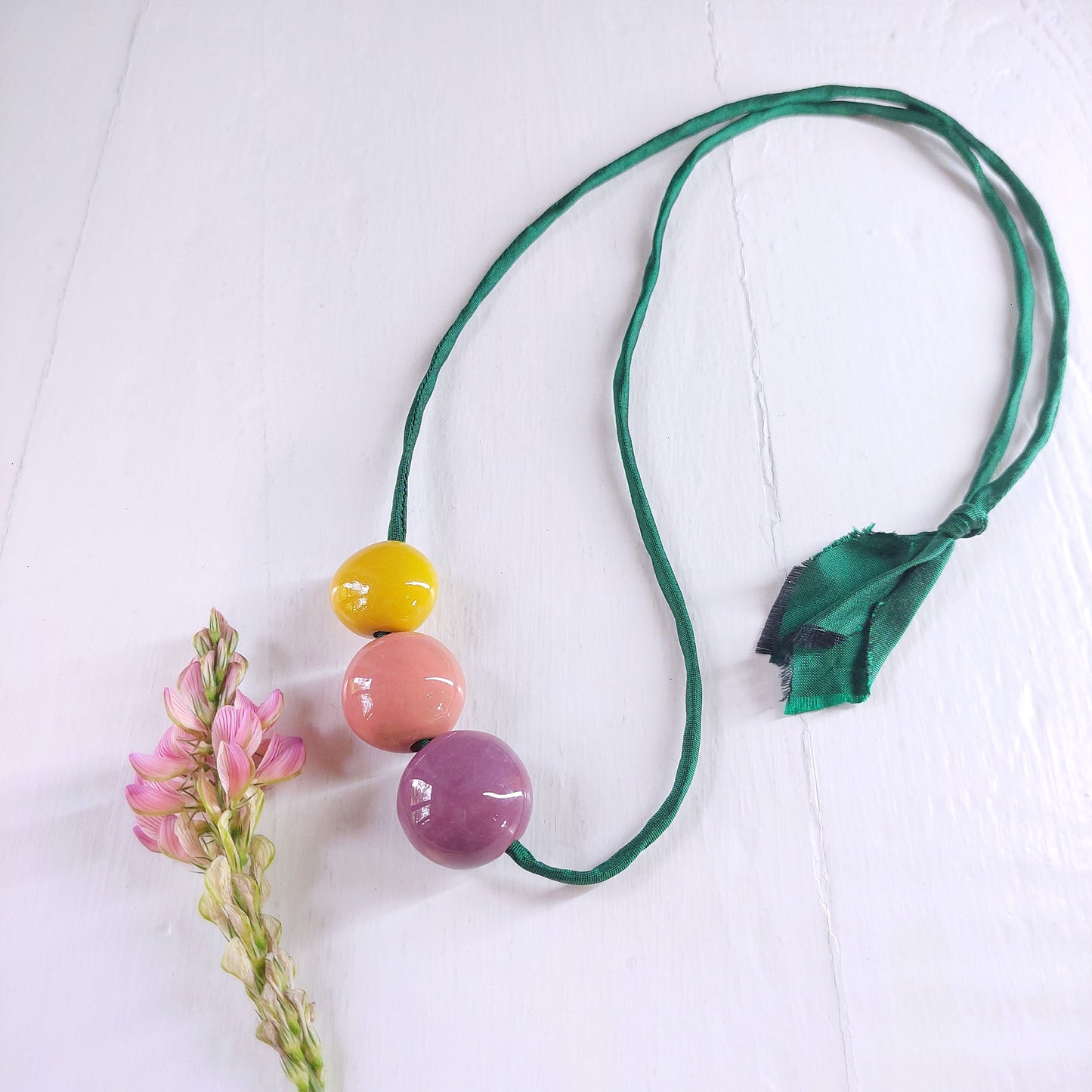 Collana da donna con tre perle in ceramica viola, rosa e gialla e laccio in seta verde.