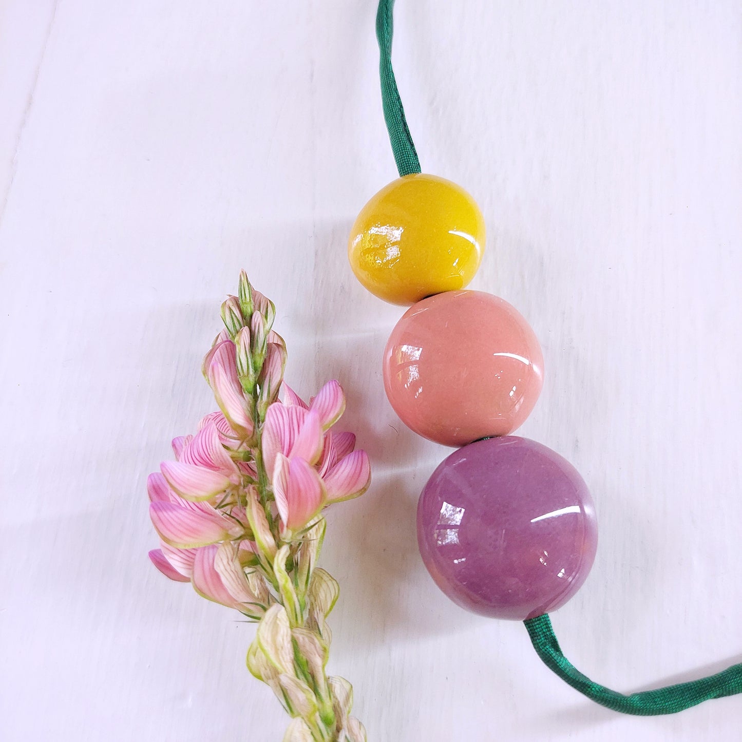 Collana da donna con tre perle in ceramica viola, rosa e gialla e laccio in seta verde.