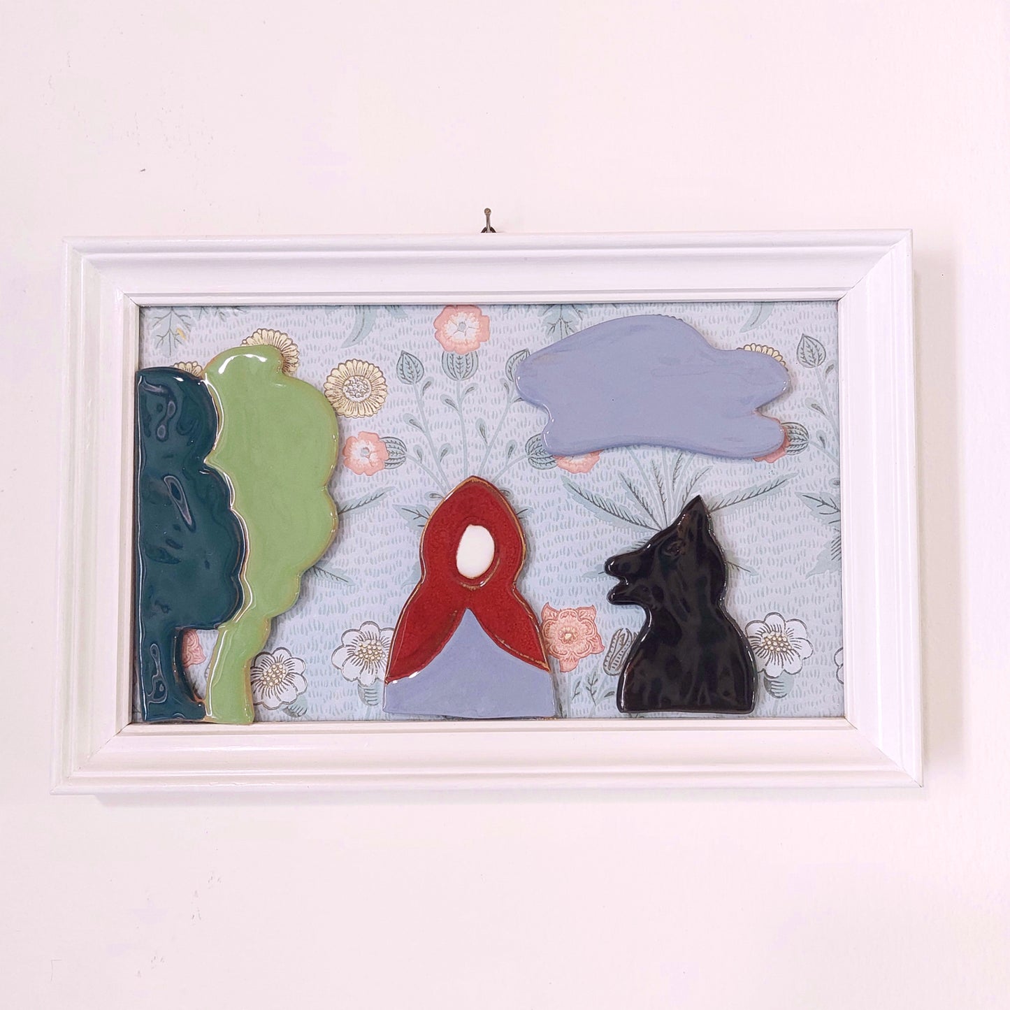 Quadro con ceramiche ispirate a Cappuccetto Rosso e cornice in legno.