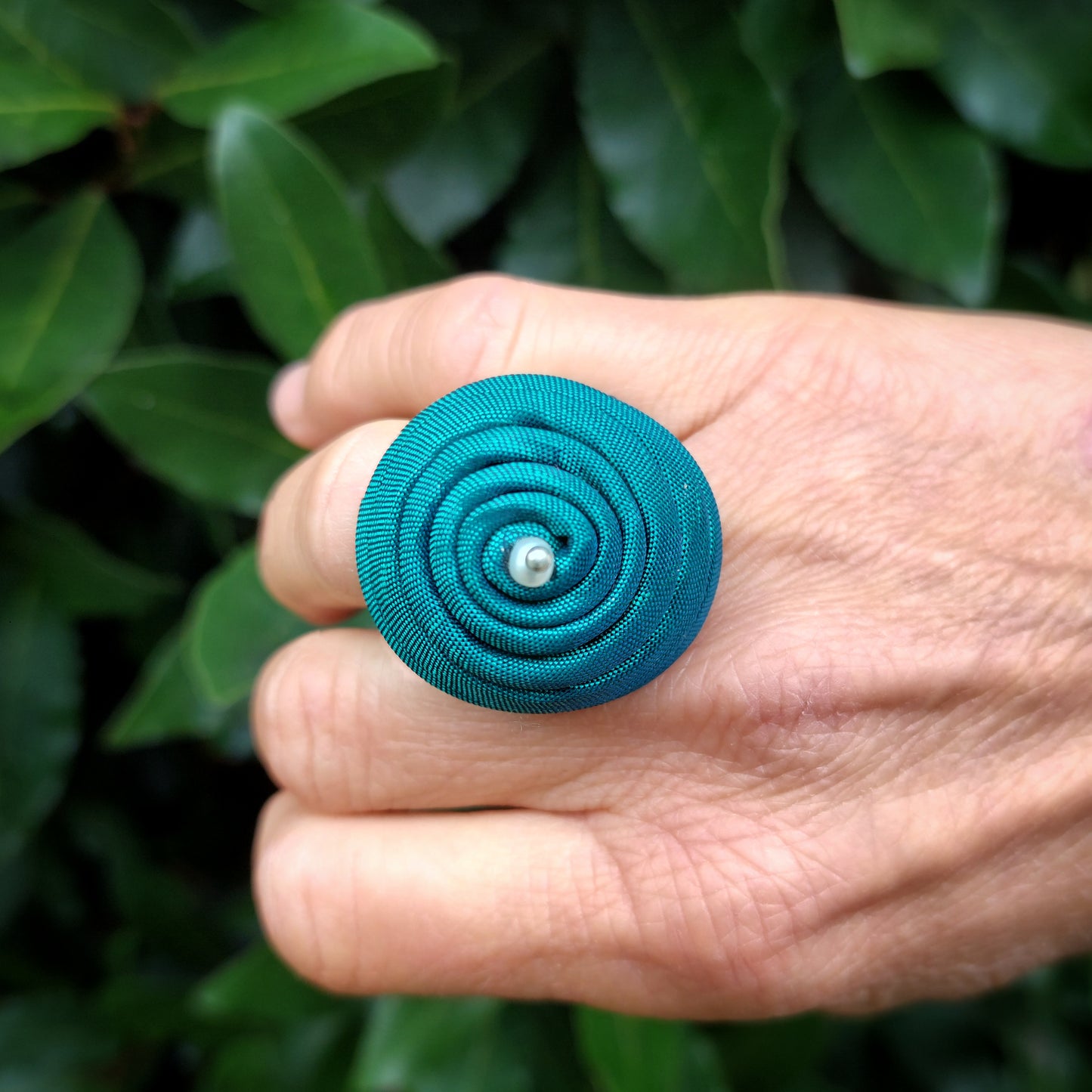 Anello bombato in tessuto verde con piccola perla bianca.