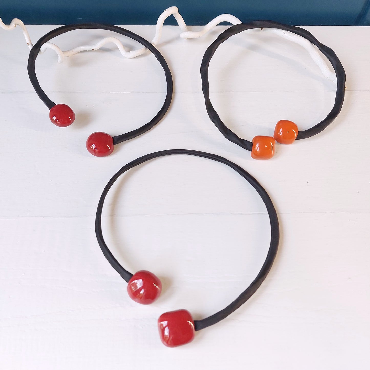 Girocollo con perle rosse quadrate in ceramica e accessorio rigido in metallo ricoperto di tessuto nero, in tre varianti colore.